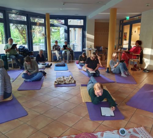 Das Bild zeigt Menschen im Rahmen eines Workshops zu Selbstfürsorge und Achtsamkeit auf Yogamatten, die etwas schreiben.